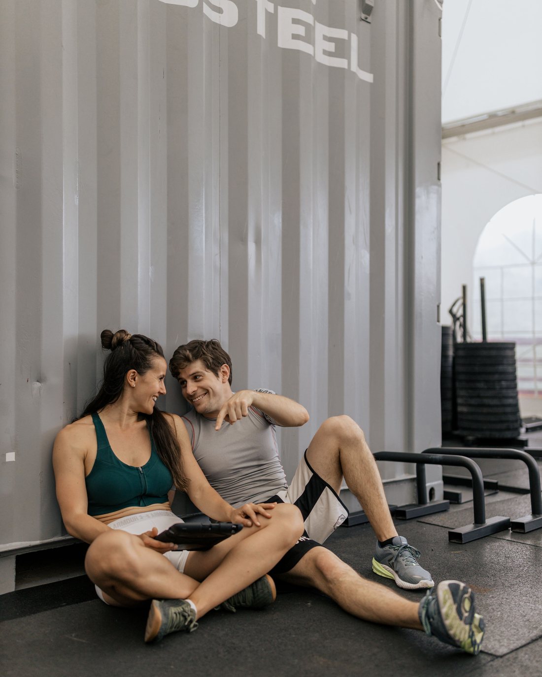 Two people sitting on the gym floor talking between sets